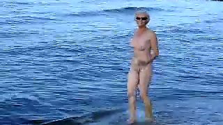 Naked old woman playing and having fun on the beach